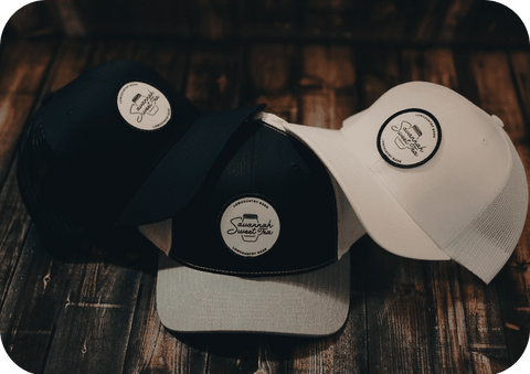 Three Savannah Sweet Tea trucker hats displayed against a textured wooden background, showcasing the variety and distinct style of our Southern-inspired headwear collection.